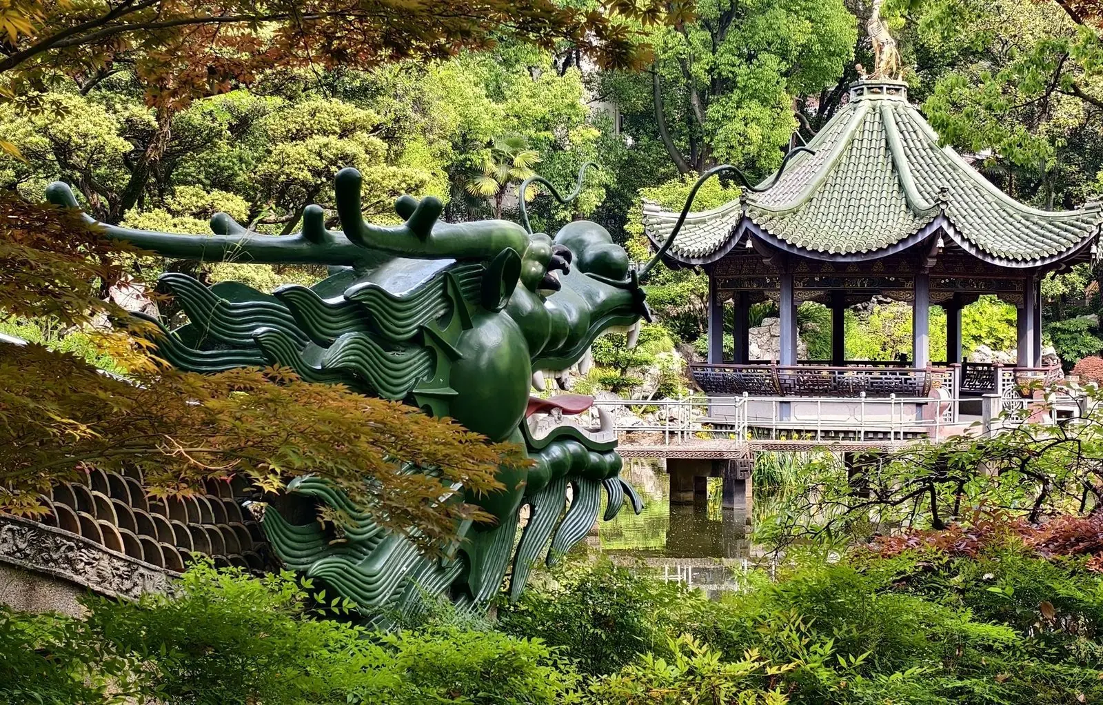 A classical Shanghai garden with a green dragon sculpture and a traditional pavilion among lush trees